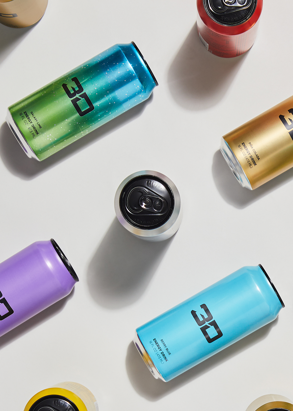 Artistically placed energy drink cans with "3D" branding in a range of flavors are displayed in an overhead arrangement.