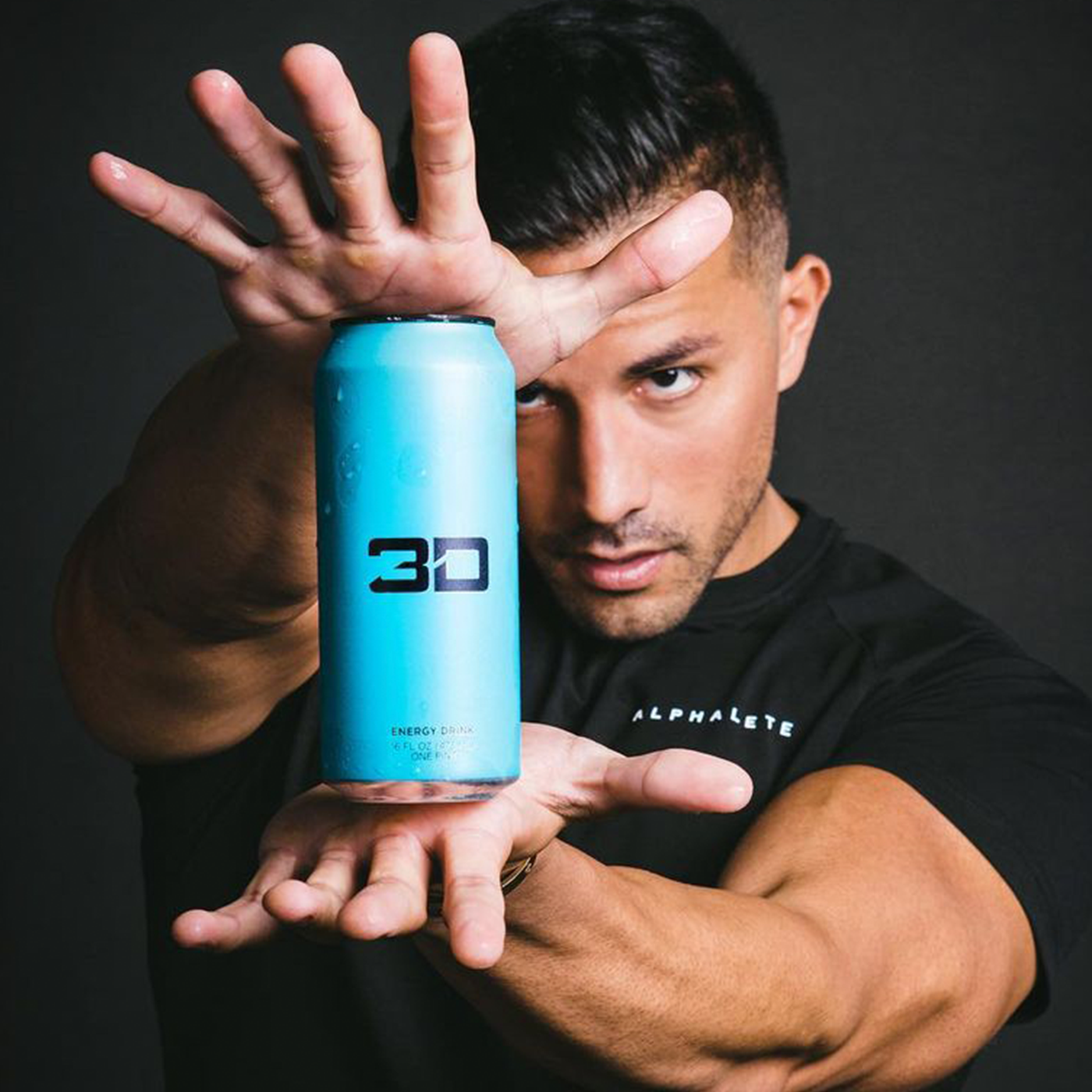 With a confident stance, Christian holds up a berry blue flavored 3D Energy drink, his hand artfully emphasizing the can in a lively gesture that draws attention to the vibrant product.