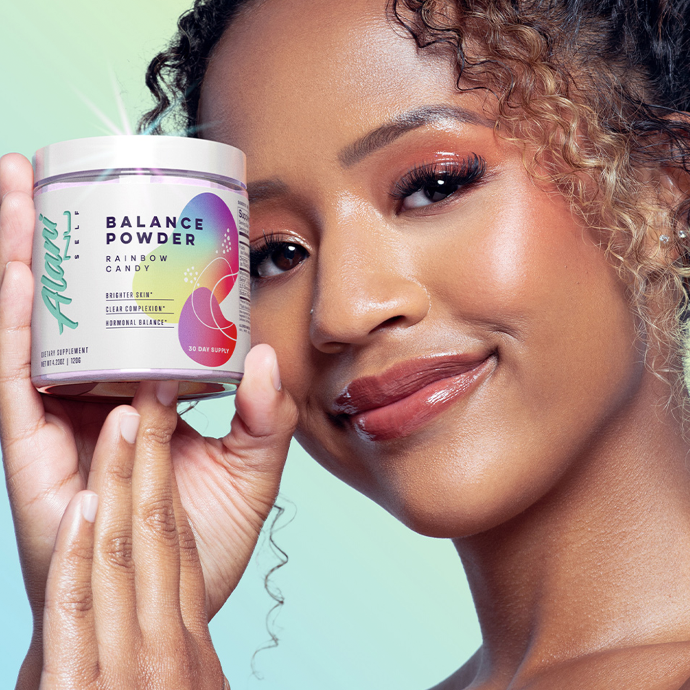 A smiling woman holding up a container of Alani Balance Powder in Rainbow Candy flavor, highlighting the product's benefits for brighter skin and hormonal balance, with a radiant, confident demeanor.
