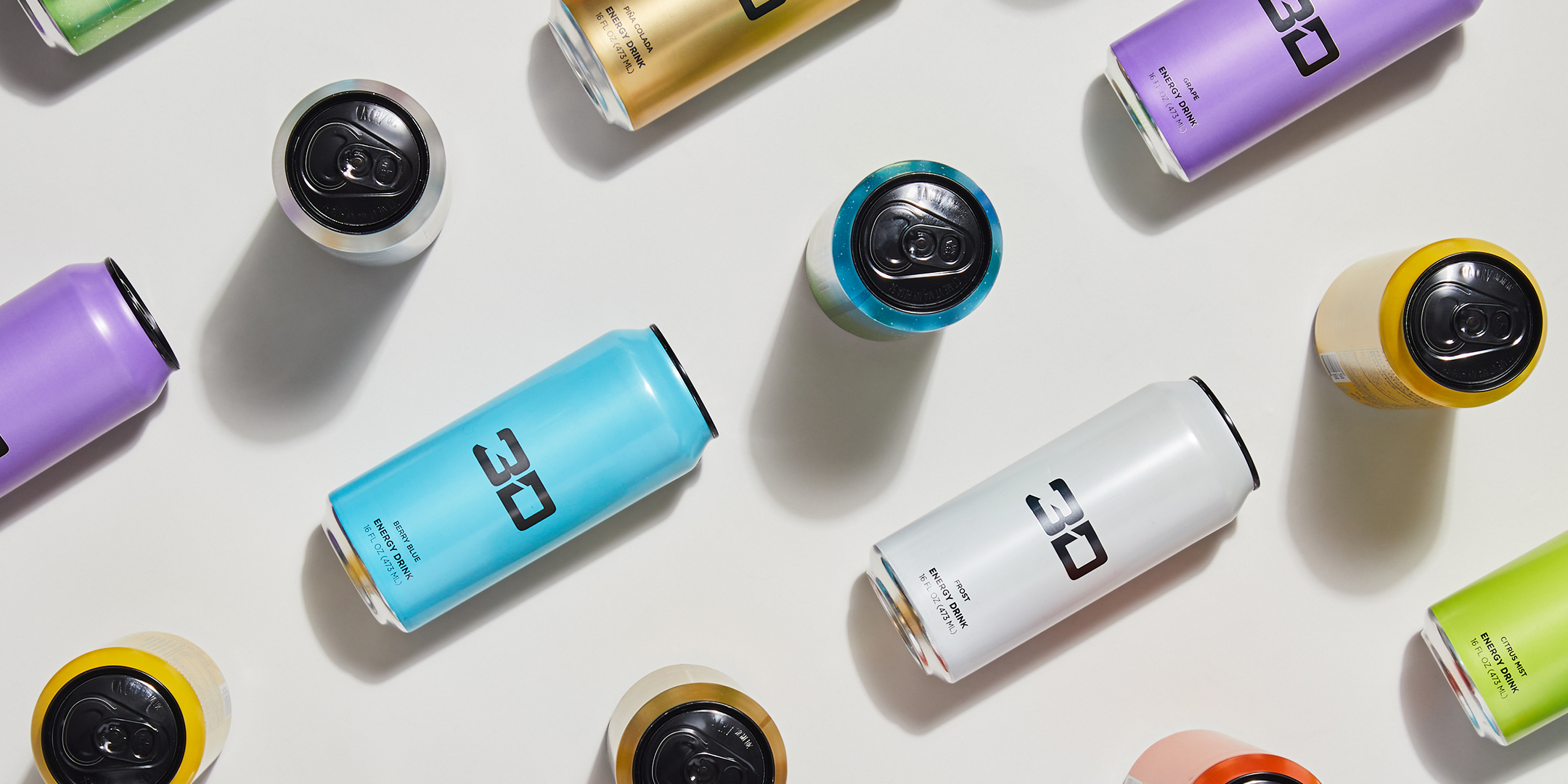 Artistically placed energy drink cans with "3D" branding in a range of flavors are displayed in an overhead arrangement.